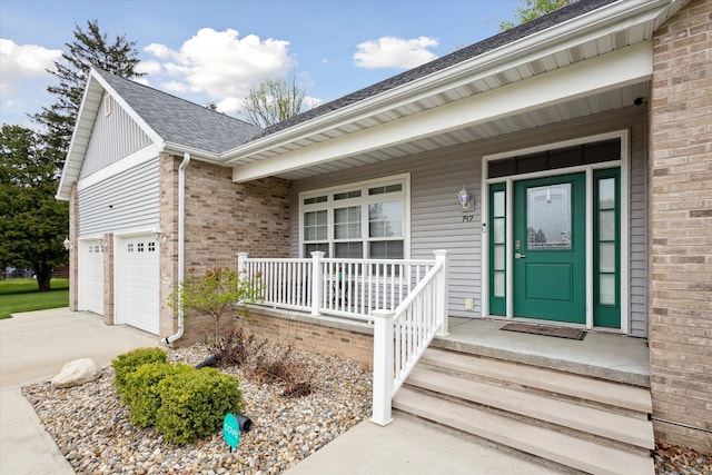 doorway to property featuring a porch, roof with shingles, brick siding, driveway, and a garage