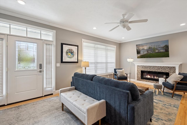 living area featuring wood finished floors, ornamental molding, recessed lighting, ceiling fan, and a glass covered fireplace