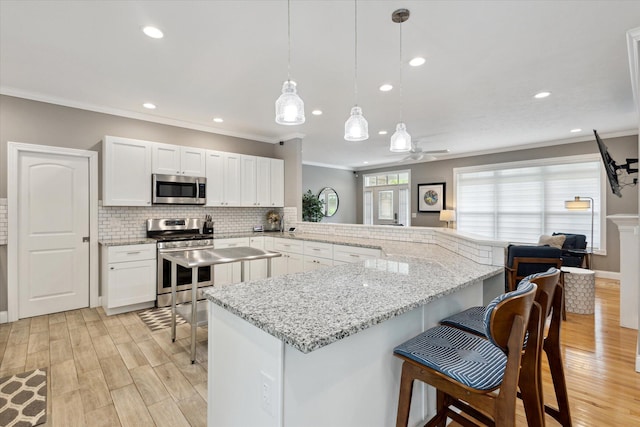 kitchen with light wood finished floors, ornamental molding, stainless steel appliances, and a breakfast bar area