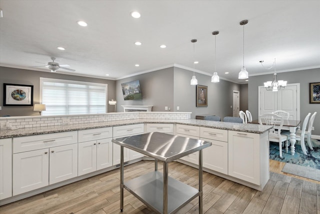 kitchen with light wood-style floors, ornamental molding, ceiling fan with notable chandelier, and white cabinets