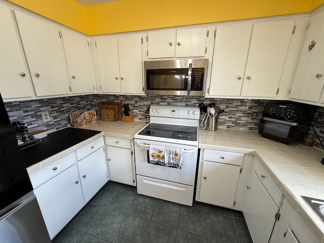 15183 Yale Rd, Lynn, MI 48097 - kitchen with white electric range, stainless steel microwave, dark tile patterned flooring, decorative backsplash, and tile counters