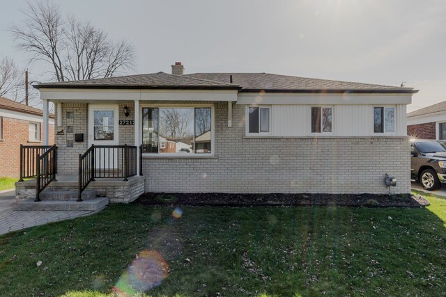 view of front of property featuring a chimney, a front yard, and brick siding