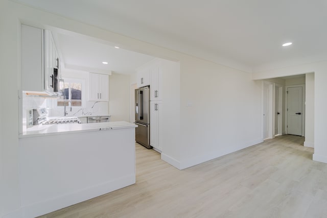 kitchen featuring light wood-style flooring, backsplash, light countertops, appliances with stainless steel finishes, and recessed lighting
