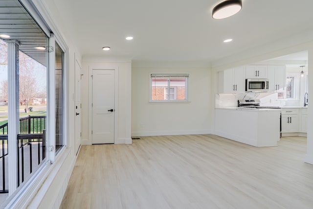 kitchen featuring light wood finished floors, white cabinetry, stainless steel microwave, baseboards, and light countertops