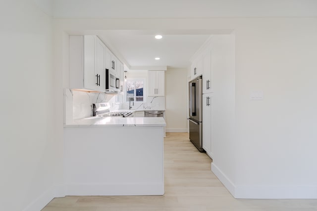 kitchen with a peninsula, stainless steel appliances, light wood-type flooring, light countertops, and white cabinets