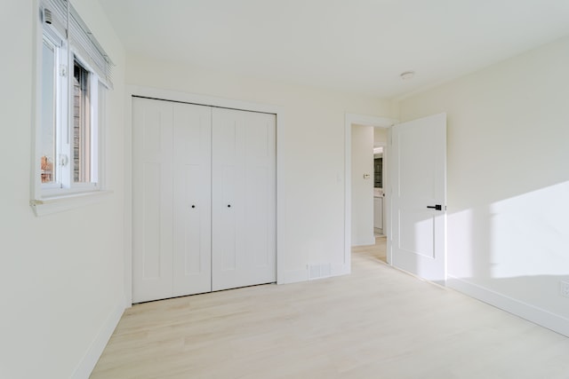 unfurnished bedroom with baseboards, a closet, visible vents, and wood finished floors