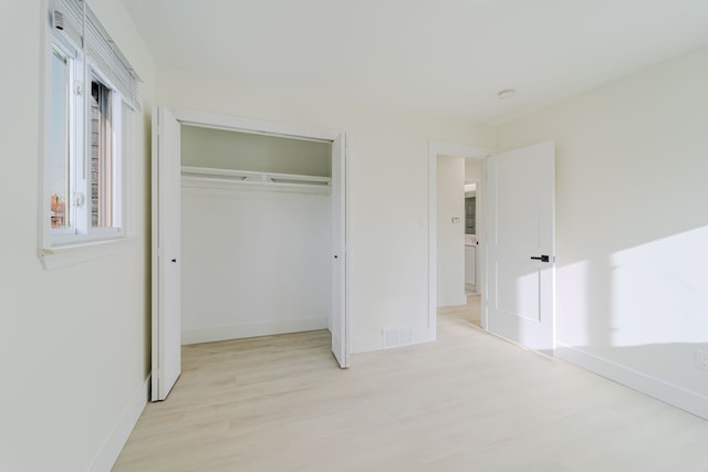 unfurnished bedroom with baseboards, light wood finished floors, a closet, and visible vents