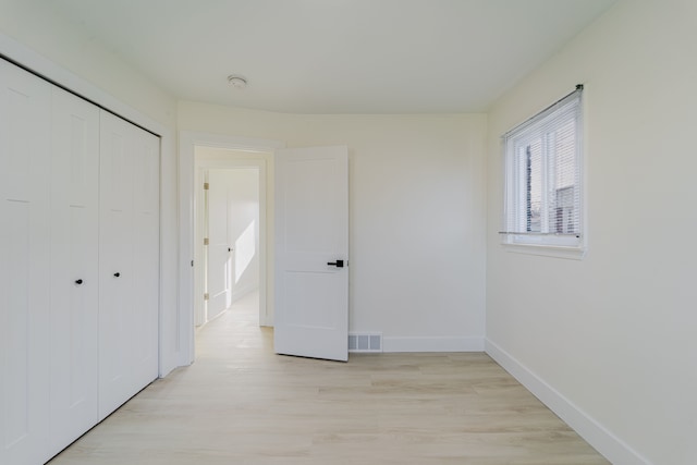 unfurnished bedroom with a closet, light wood-style floors, visible vents, and baseboards