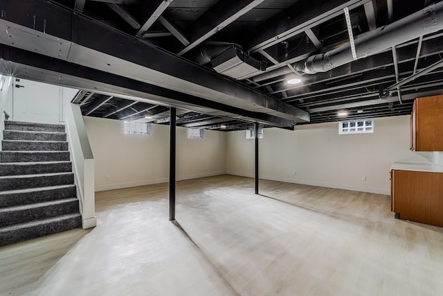 below grade area featuring baseboards, stairway, and light wood finished floors
