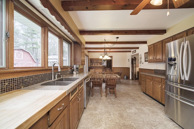 kitchen featuring decorative light fixtures, stone finish flooring, a sink, beamed ceiling, and stainless steel appliances