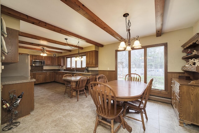 dining space with a ceiling fan, beam ceiling, wood walls, and wainscoting