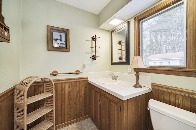 half bath featuring a wainscoted wall, toilet, wooden walls, and vanity