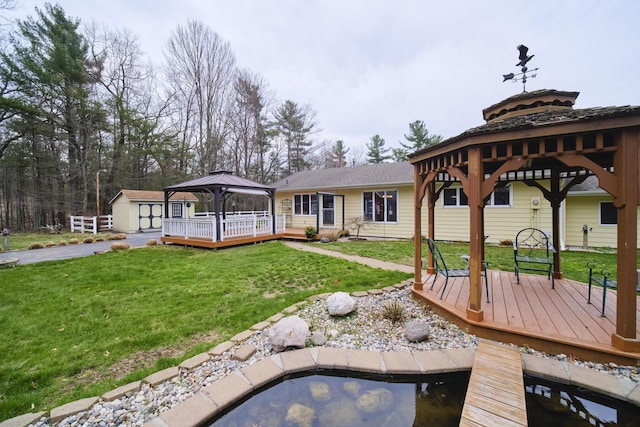 back of property featuring a lawn, a wooden deck, a gazebo, a shed, and an outbuilding