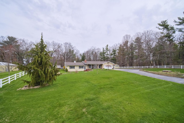 ranch-style home featuring a chimney, aphalt driveway, a front lawn, and fence