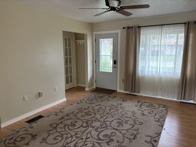 foyer entrance with baseboards, ceiling fan, visible vents, and wood finished floors
