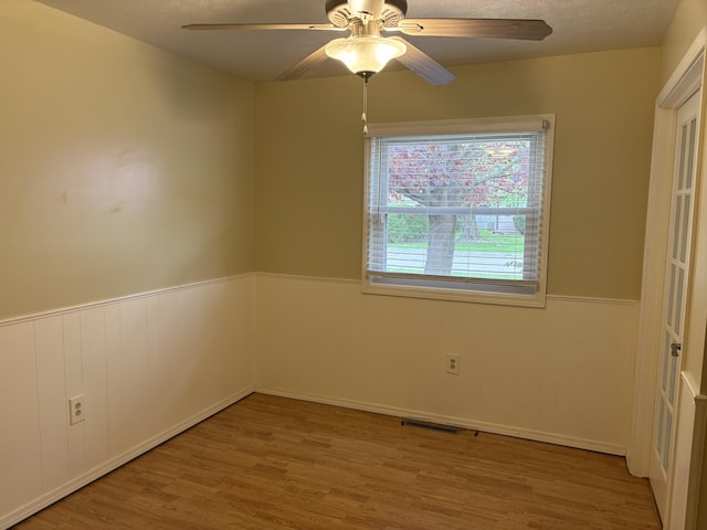 interior space featuring a ceiling fan, visible vents, a wainscoted wall, and wood finished floors