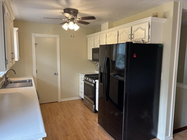 kitchen featuring a sink, black appliances, ceiling fan, light wood-style flooring, and white cabinets