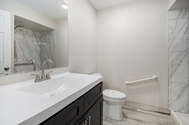 bathroom featuring a tile shower, toilet, and vanity