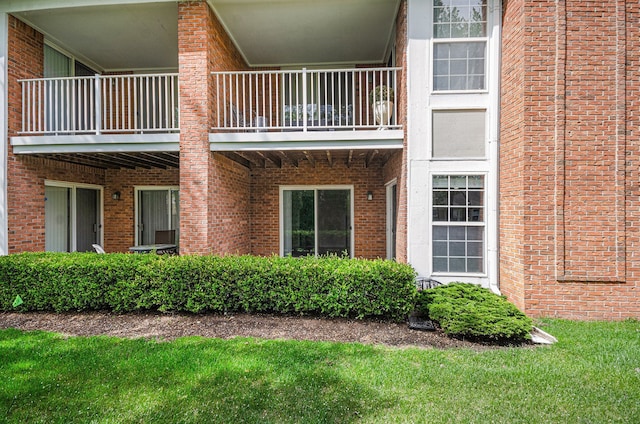 view of home's exterior with a balcony, brick siding, and a yard