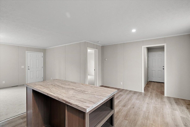 kitchen with light wood-type flooring, a textured ceiling, crown molding, and a center island