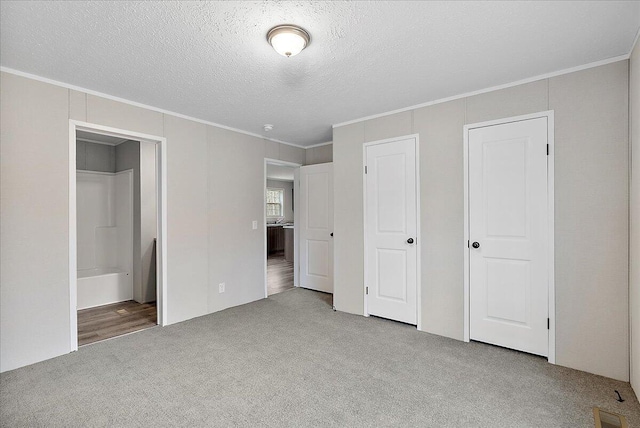 unfurnished bedroom with a textured ceiling, carpet flooring, ensuite bathroom, ornamental molding, and visible vents
