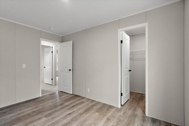 unfurnished bedroom with light wood finished floors, crown molding, a closet, and a walk in closet