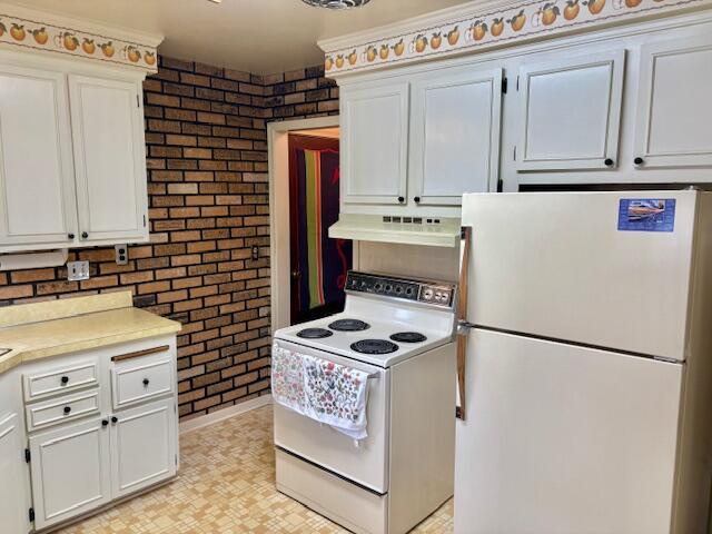 kitchen featuring white appliances, under cabinet range hood, light countertops, white cabinets, and brick wall