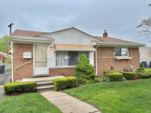 view of front of home featuring a front lawn, brick siding, a chimney, and fence