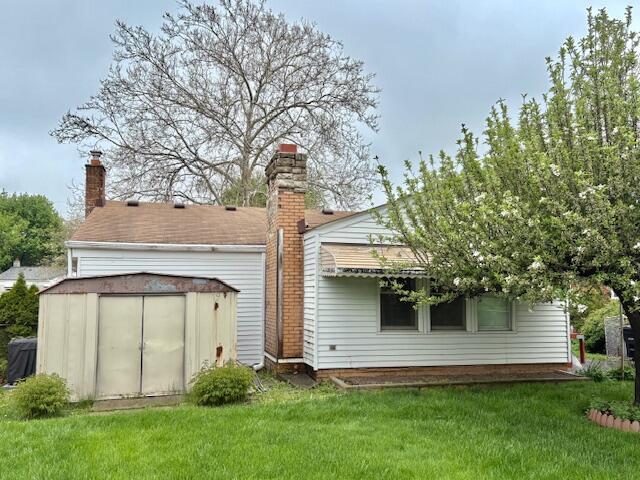 back of house with a chimney and a lawn