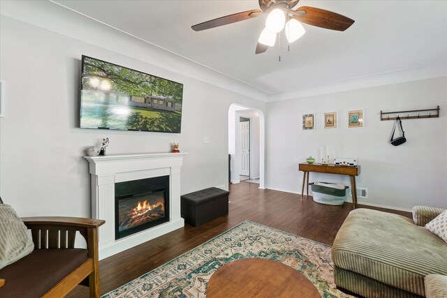 living area featuring wood finished floors, arched walkways, ceiling fan, and a glass covered fireplace
