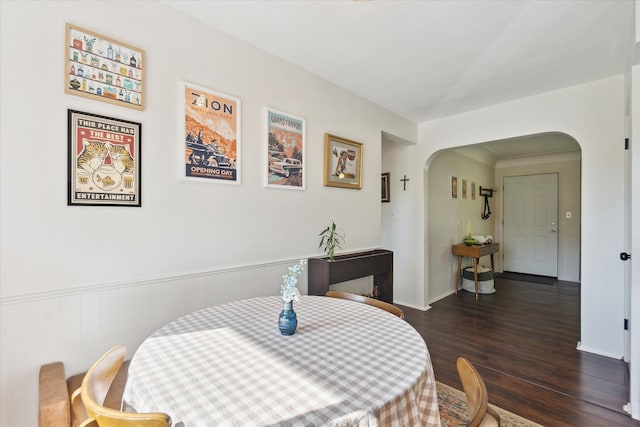 dining space featuring arched walkways and wood finished floors