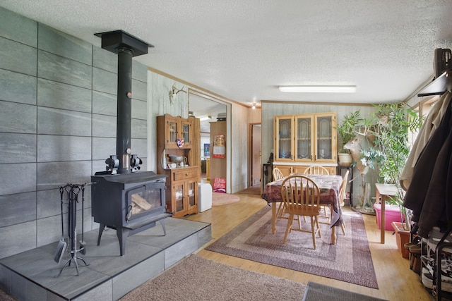 dining room featuring a wood stove, wooden walls, a textured ceiling, and wood finished floors