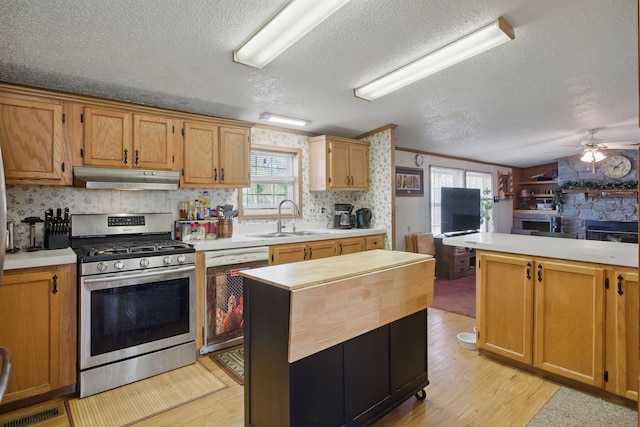 kitchen featuring under cabinet range hood, light countertops, stainless steel range with gas stovetop, and a sink
