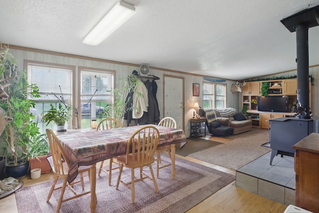 dining room with a wood stove, plenty of natural light, light wood-type flooring, and a textured ceiling