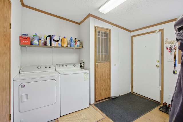 clothes washing area featuring washing machine and dryer, wood finished floors, laundry area, a textured ceiling, and ornamental molding