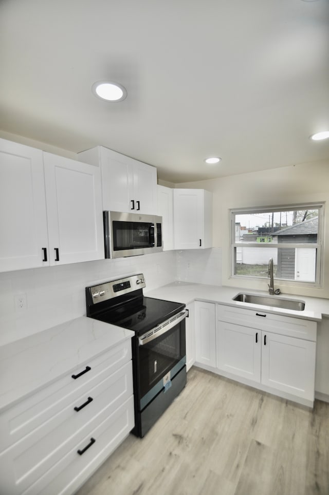 kitchen with stainless steel appliances, a sink, white cabinets, light wood-style floors, and light stone countertops