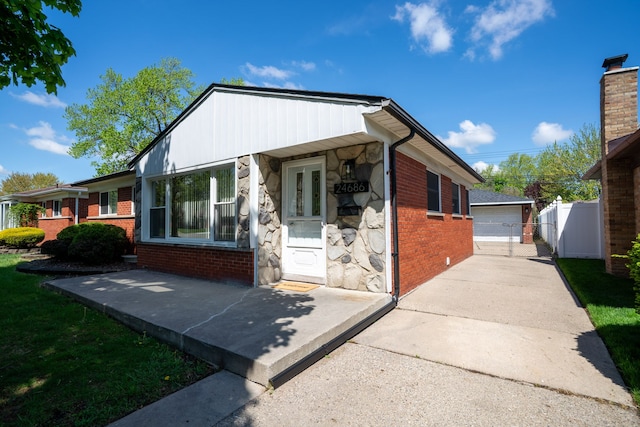 view of front of property featuring brick siding, stone siding, a detached garage, an outbuilding, and fence