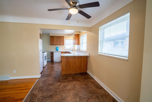 kitchen featuring brown cabinetry, white appliances, a sink, baseboards, and ceiling fan
