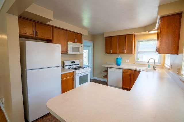 kitchen with white appliances, a sink, brown cabinetry, and a peninsula
