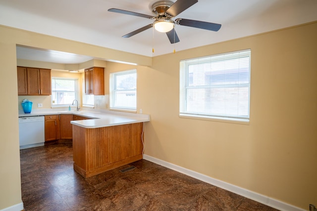 kitchen with white dishwasher, a peninsula, brown cabinetry, a sink, and baseboards
