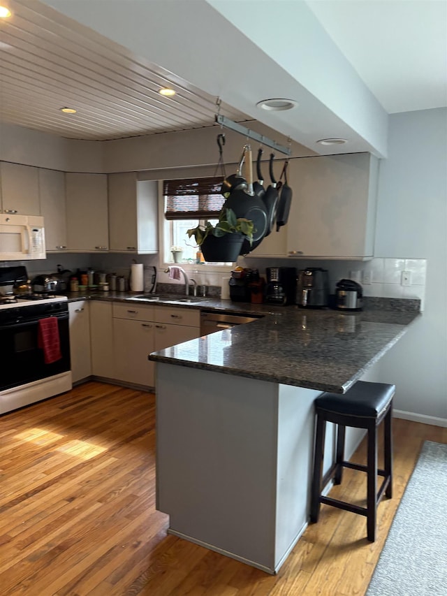 kitchen with a sink, a peninsula, white microwave, light wood-type flooring, and gas stove