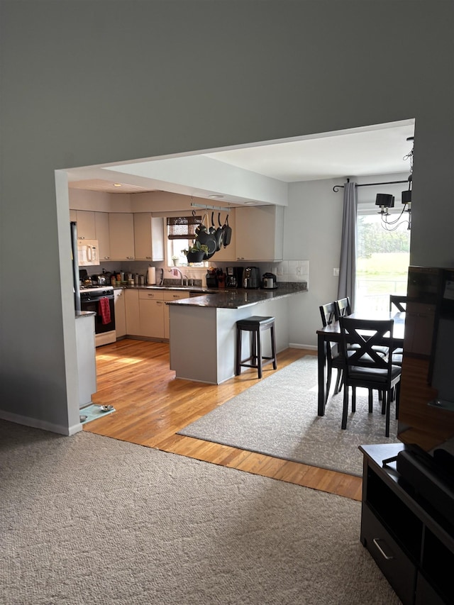 kitchen with a peninsula, a breakfast bar, dark countertops, a notable chandelier, and white appliances
