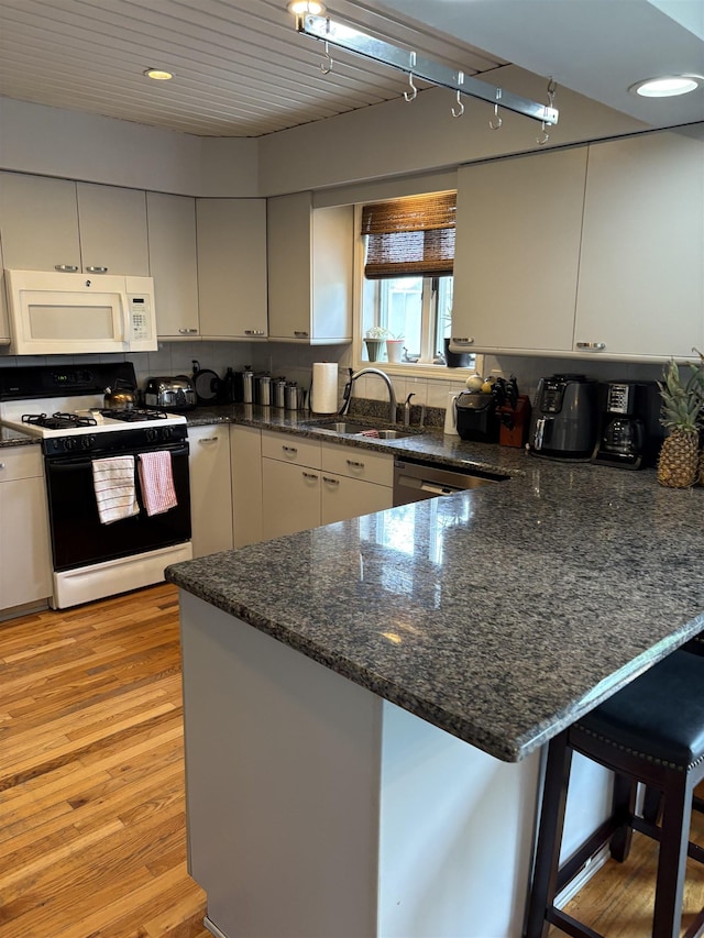 3470 Seymour Rd, Swartz Creek, MI 48473 - kitchen featuring white microwave, black gas range, a peninsula, light wood-style flooring, and dark stone counters