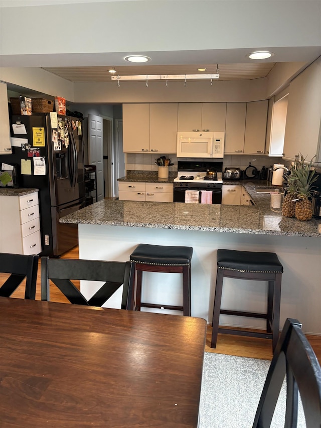 3470 Seymour Rd, Swartz Creek, MI 48473 - kitchen with white microwave, range, black fridge, a peninsula, and tasteful backsplash