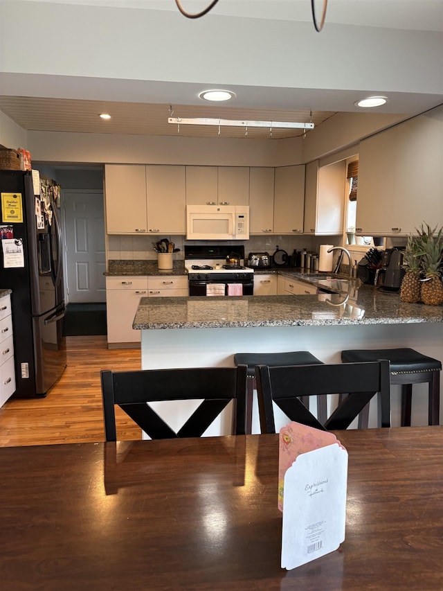 3470 Seymour Rd, Swartz Creek, MI 48473 - kitchen featuring white microwave, fridge with ice dispenser, range with gas cooktop, a peninsula, and a kitchen bar