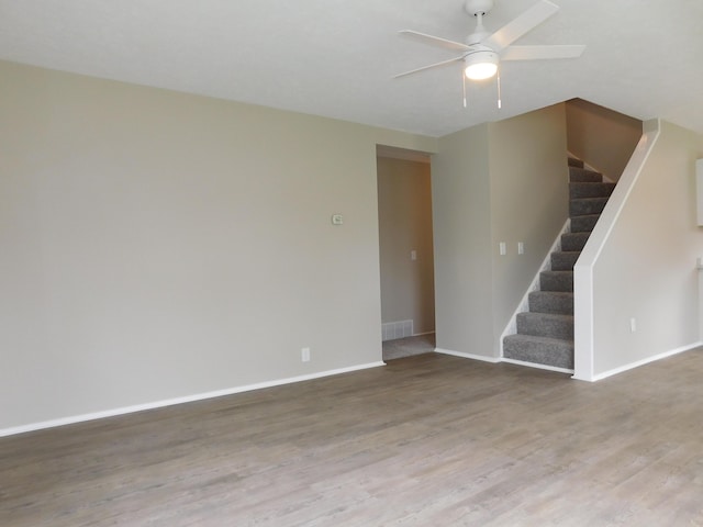 empty room featuring wood finished floors, stairway, baseboards, visible vents, and ceiling fan