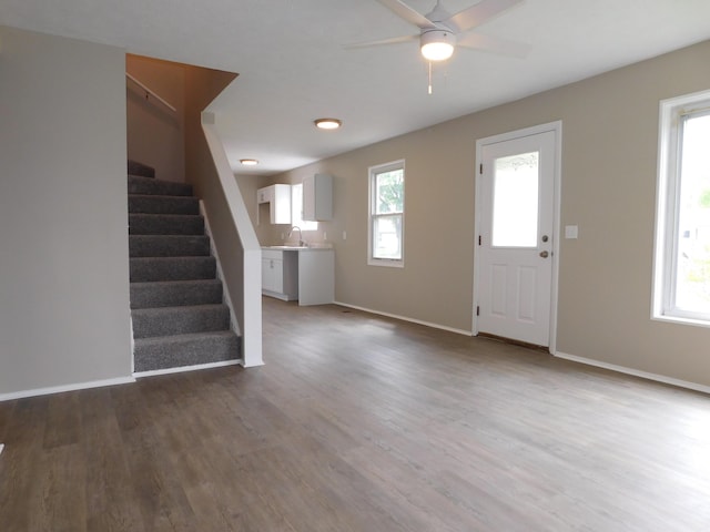 unfurnished living room featuring baseboards, ceiling fan, a sink, wood finished floors, and stairway