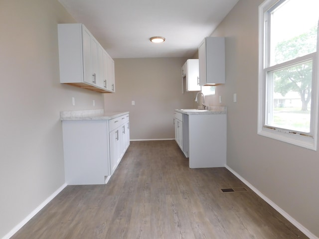 kitchen featuring a sink, light wood finished floors, light countertops, and baseboards