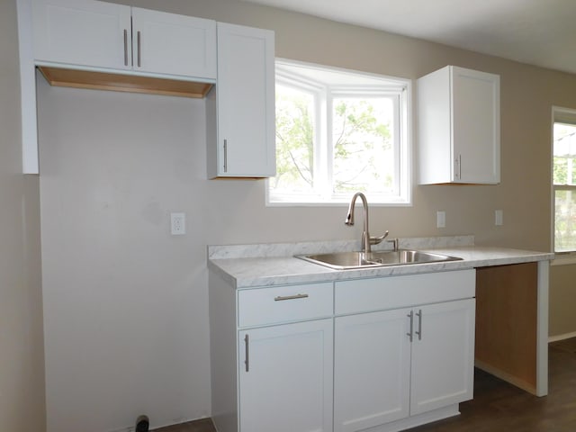 kitchen with a sink, white cabinetry, dark wood-type flooring, baseboards, and light countertops