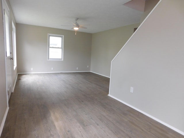 unfurnished room with baseboards, dark wood-style flooring, a ceiling fan, and stairs